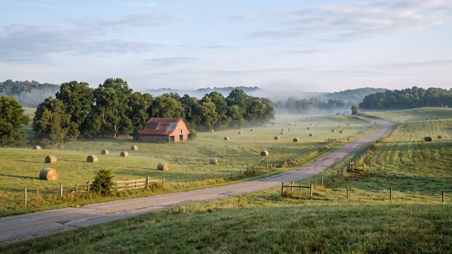 Rolling Maury County hayfields with round bales, a red barn and morning mist