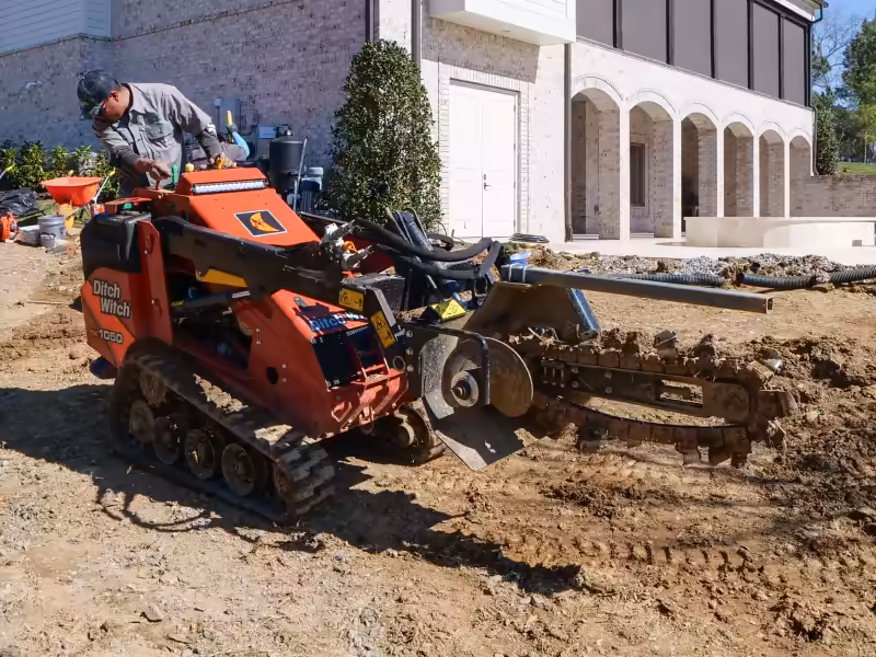 Trencher cutting an irrigation line beside a new home