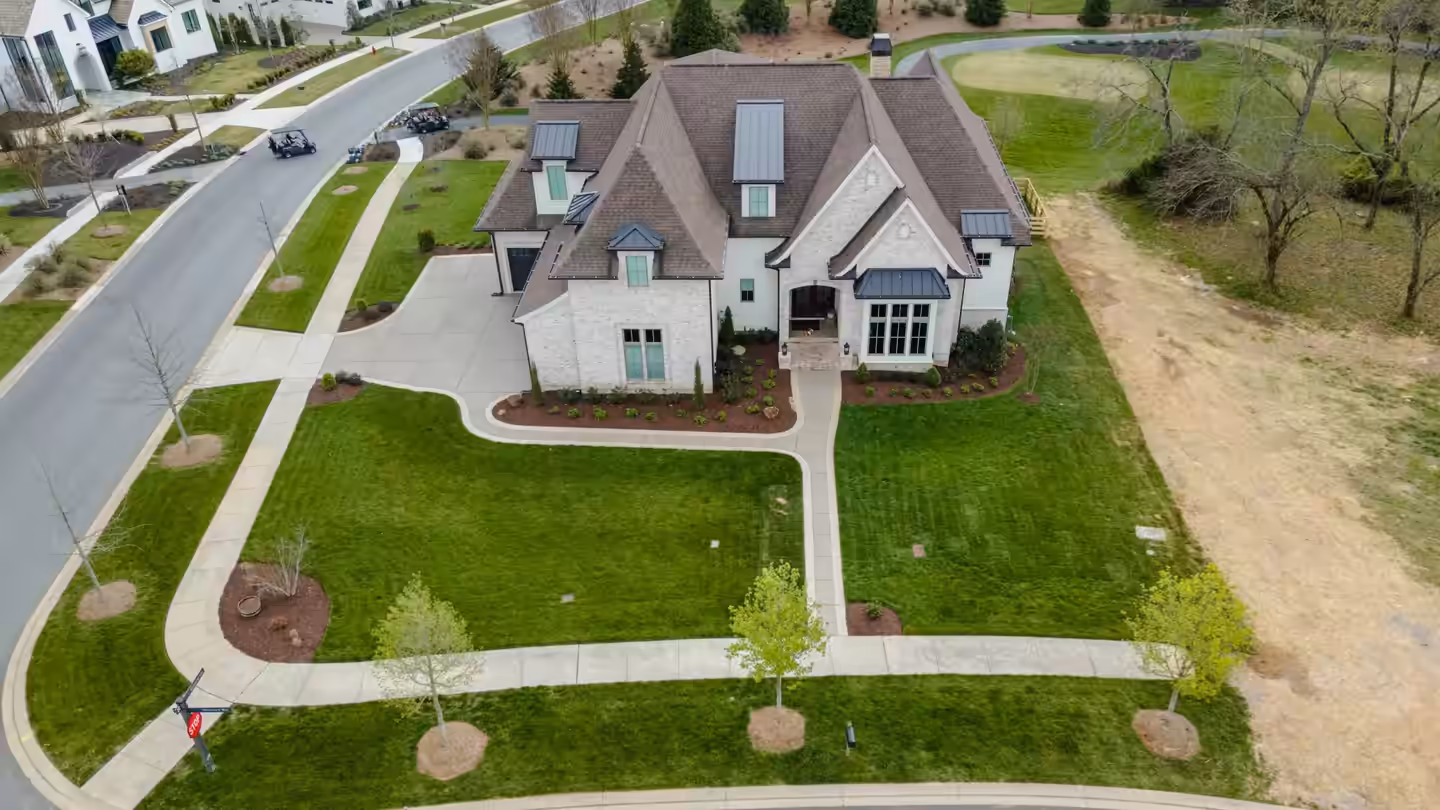 Aerial view of a new home's finished front yard with curving walkways, fresh sod, young trees and planted foundation beds