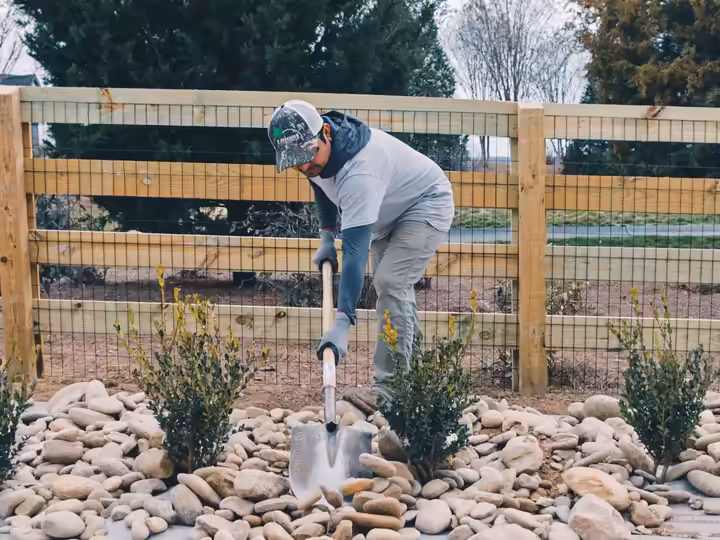 Richardson crew member planting shrubs in a river-rock bed along a farm fence