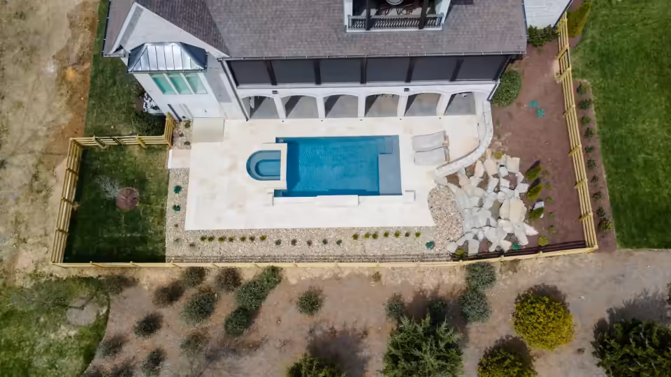 Aerial view of a pool with a travertine deck, boulders and new planting