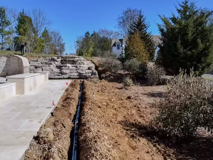 A drain line runs beside the new terrace and boulder wall, so water leaves the yard.