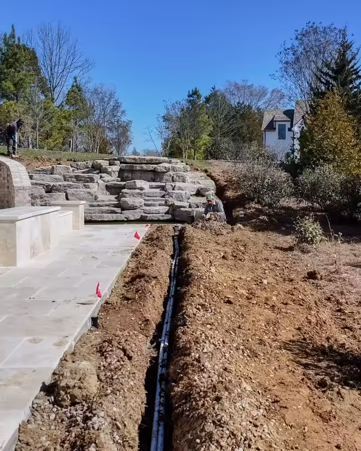 Drain line trench running beside a new stone terrace and planting at a Middle Tennessee home