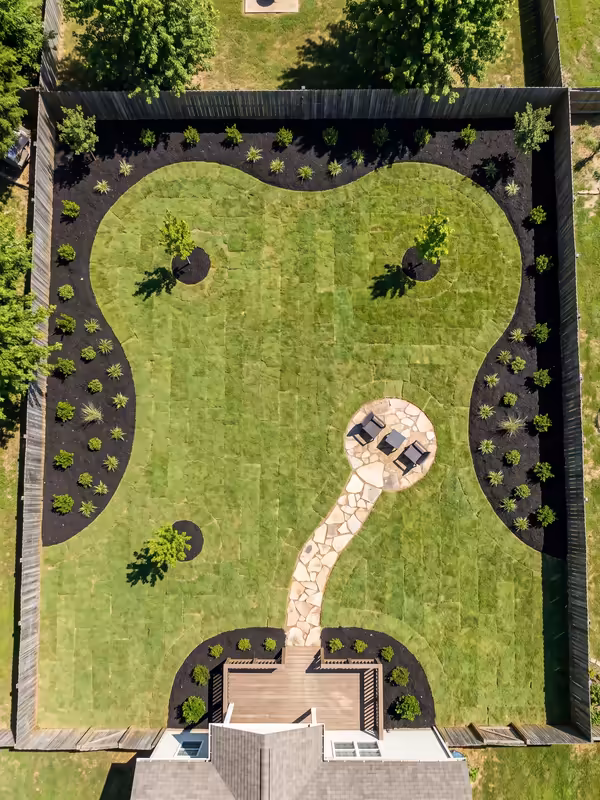 Aerial view of a newly planted backyard with curving beds, fresh sod and a stone path