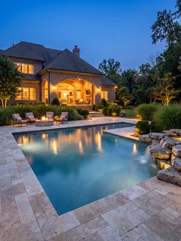 Travertine pool deck with a boulder water feature and fire pit at dusk