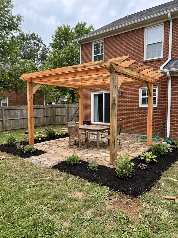 New cedar pergola over a flagstone patio behind a brick home, with fresh mulch beds and young plants