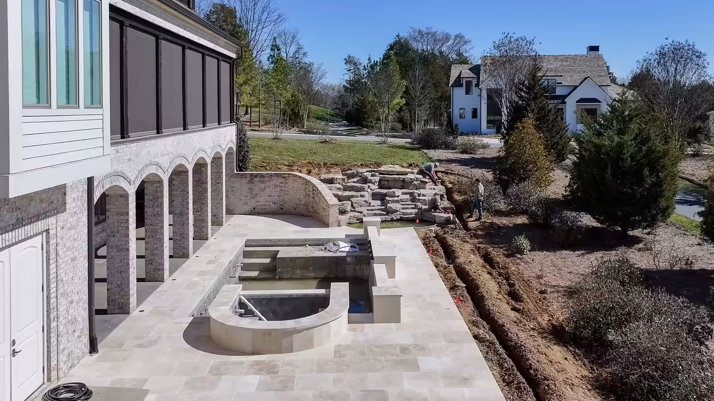Travertine terrace with a raised spa below arched loggias, boulder steps and a new drain line at a Middle Tennessee home