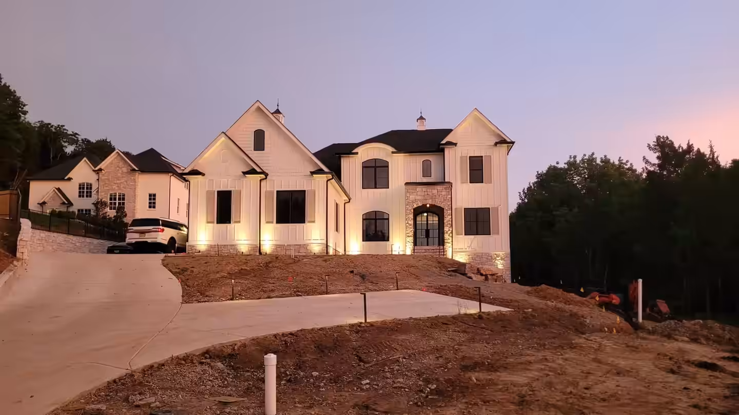 Large new home at dusk with warm uplighting across the facade
