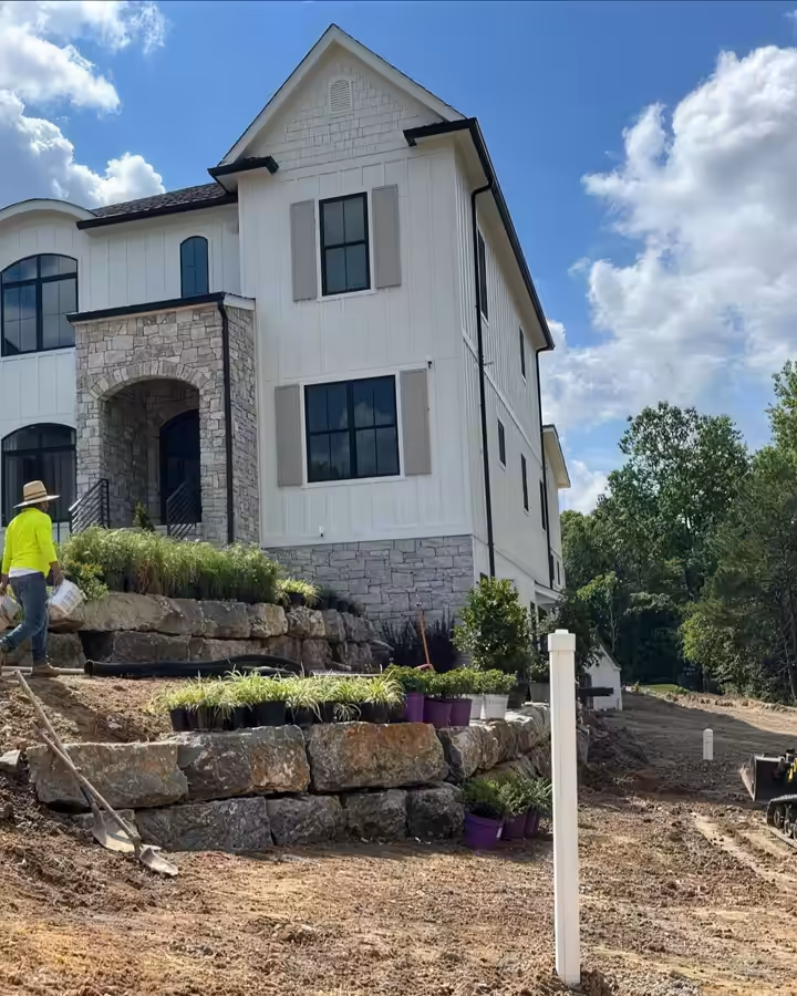 Richardson crew building stacked-stone retaining walls and steps below a new white home